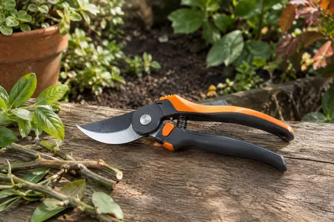 Sécateur manuel noir et orange à poignée tournante posé près de rameaux frais dans un jardin
