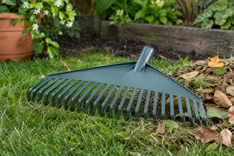 Tête de balai-râteau en plastique posée près de feuilles et de résidus de tonte dans un jardin.