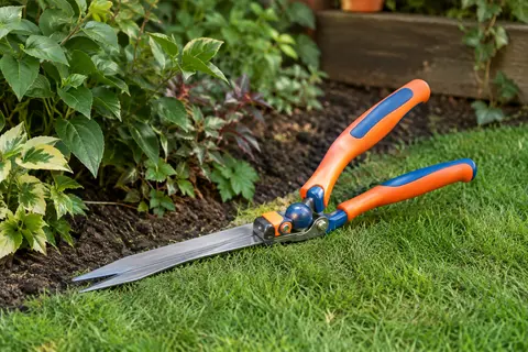 Cisaille à gazon orientable aux lames argentées et poignées orange et bleues, posée près d’une bordure.