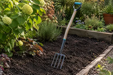 Fourche à bêcher Gardena à manche en frêne et poignée en D posée près d’un massif de terre ameublie.