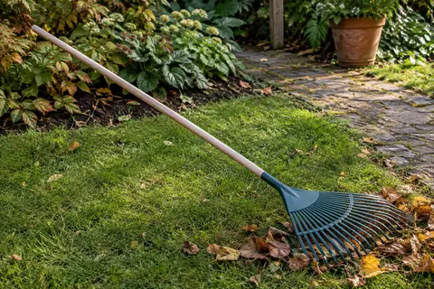 Balai à gazon Leborgne à 27 dents, tête en polymère et manche en bois posé près de feuilles rassemblées