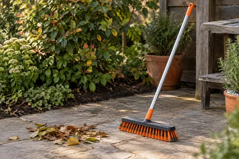 Balai de jardin Lifewit orange à manche long, posé près d’une terrasse et de feuilles balayées.