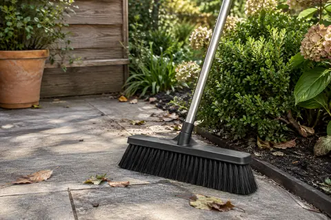 Balai-brosse noir à tête large et manche en acier inoxydable posé sur une terrasse.