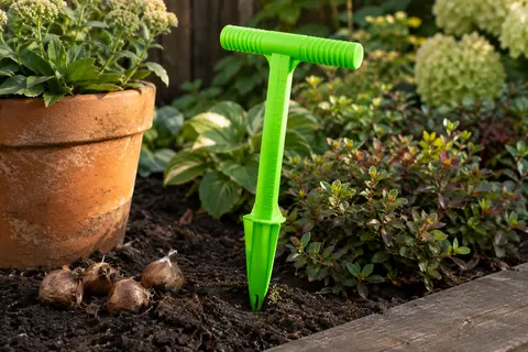 Plantoir à bulbes Milifox vert fluorescent avec poignée en T et échelle, posé près de bulbes dans la terre.