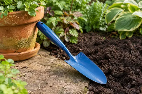 Transplantoir tout acier bleu posé près d’une jardinière, avec sa lame dans la terre sombre.