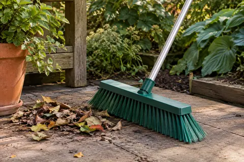 Balai d’extérieur vert à manche long et tête angulaire posé sur une terrasse de jardin