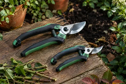 Deux sécateurs Workpro noirs et verts, un modèle de jardin et un petit sécateur à fleurs posés sur du bois.