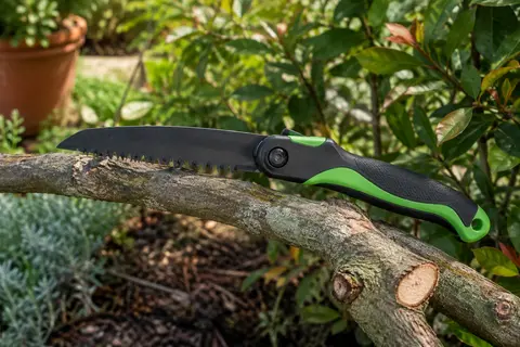 Scie d’élagage pliante Workpro à lame sombre et poignée noire et verte, posée sur une branche coupée.